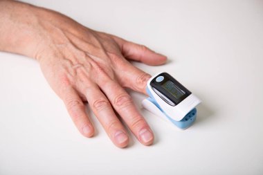 Middle aged man measuring blood oxygen saturation with a digital oximeter at home. 