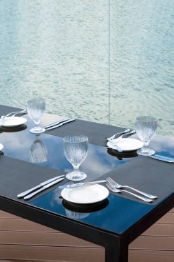 Plaj restoranındaki masada kristal boş bardaklar, beyaz tabaklar ve çatal bıçak takımı. Şenlikli bir akşam yemeği için masa hazırlıyorum..