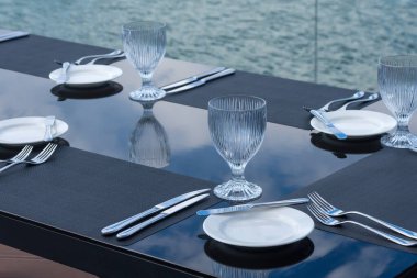 Plaj restoranındaki masada kristal boş bardaklar, beyaz tabaklar ve çatal bıçak takımı. Şenlikli bir akşam yemeği için masa hazırlıyorum..