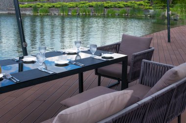 Plaj restoranındaki masada kristal boş bardaklar, beyaz tabaklar ve çatal bıçak takımı. Şenlikli bir akşam yemeği için masa hazırlıyorum..