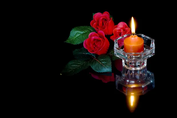 Горящая свеча и три красных розы на черном фоне — стоковое фото