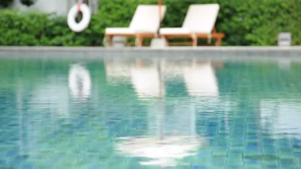 Agua ondulada en la piscina con sillas de playa y fondo de planta verde — Vídeo de stock