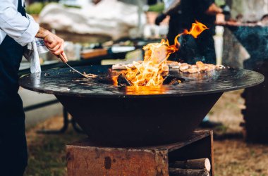 The cook cleans a round barbecue with an open fire.