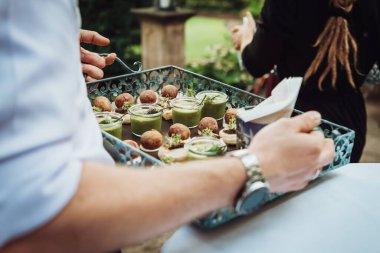 Snacks on a tray for a banquet. Green soup in small glasses