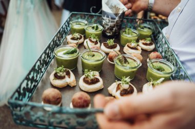 Snacks on a tray for a banquet. Green soup in small glasses