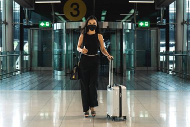 Havaalanı girişinde maskeli bir kadın var. Elinde pasaport ve dezenfektan var. Yüksek kalite fotoğraf