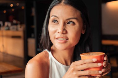 Smiling asian woman drinking a coffee in a restaurant or coffee shop. High quality photo