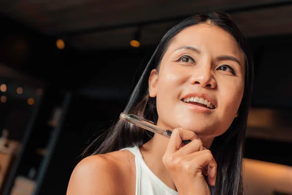 Smiling beautiful asian woman thinking and holding a pen. High quality photo