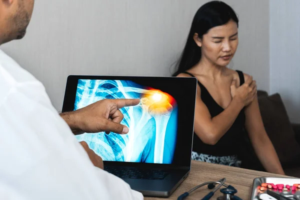 Doctor showing a x-ray of pain in the shoulder on a laptop. Woman patient holding her shoulder. High quality photo
