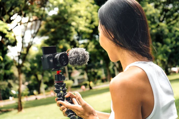 Young asian woman recording video with a camera for vlog and social media in a park. High quality photo