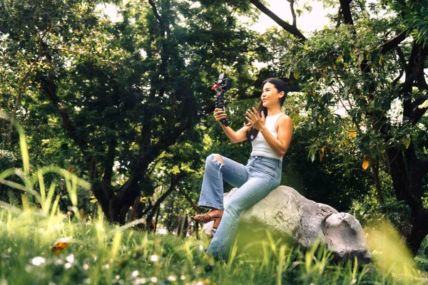 Young asian woman recording video with a camera for vlog and social media in a park. High quality photo