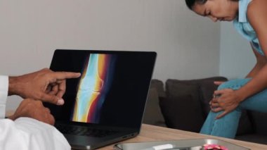 Doctor showing x-ray of pain in a knee on a laptop with woman patient. High quality 4k footage