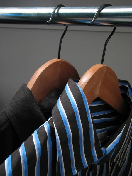 Two stylish shirts on wooden hangers — 图库照片