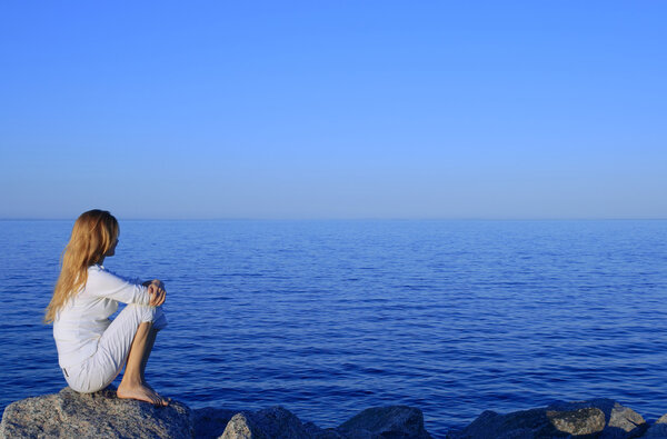 Девушка, сидящая на скале у мирного моря
