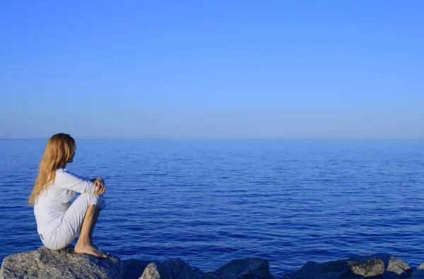 Chica sentada en la roca junto al mar apacible Imagen de stock