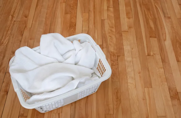 Toalhas brancas em uma cesta de lavanderia no chão de madeira — Fotografia de Stock