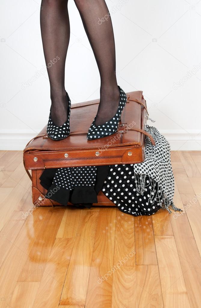 Woman in high heel shoes standing on overfilled suitcase