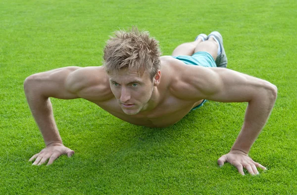 Young man doing push-ups on green grass — Stock Photo, Image