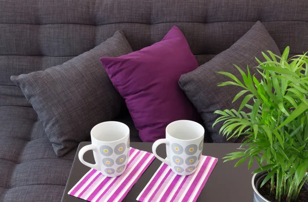 Sofá con cojines y dos tazas sobre una mesa — Foto de Stock