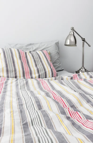 Metall lampa nära sängen med färgglada sängkläder — Stockfoto