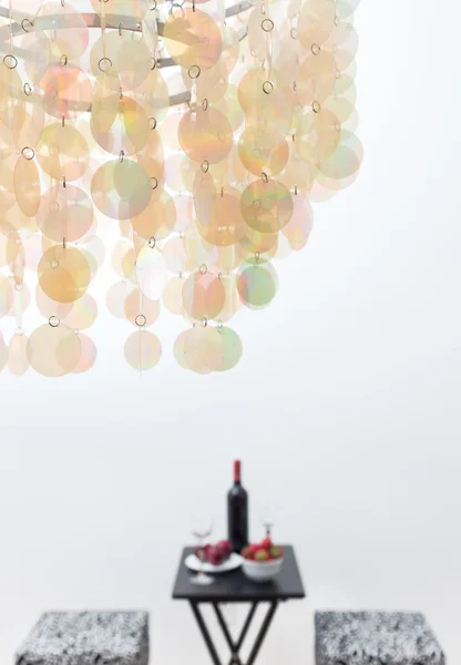 Botella de vino tinto en una mesa, hermosa lámpara de araña decorando un —  Fotos de Stock