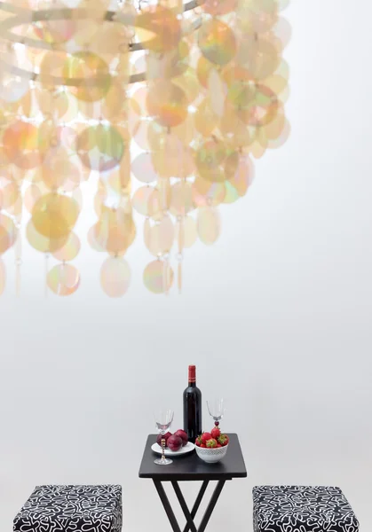 Láhev červeného vína na stůl a dekorativní lustr — Stock fotografie