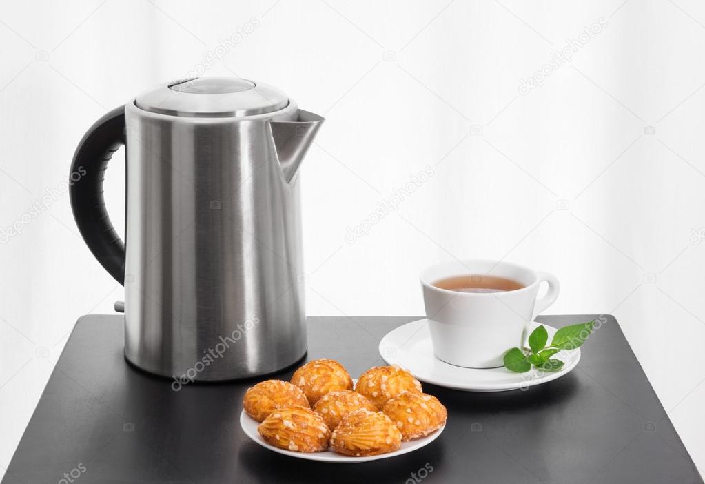 Electric kettle, cup of tea and cookies on a table