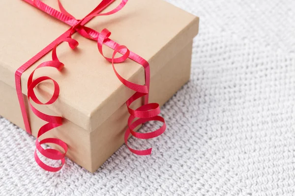 Gift with red ribbon on a knitted background — Stock Photo, Image