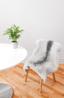 Chair covered with sheepskin, and plant on a white table clipart
