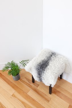 Green plant and stool covered with sheepskin in the room corner clipart