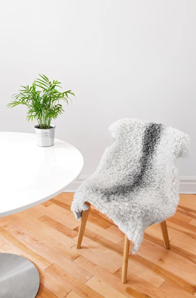 Cadeira coberta de pele de carneiro e planta em uma mesa branca — Fotografia de Stock