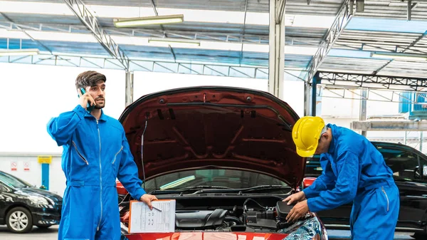 Tamirci, asistanıyla birlikte açık kaput vagonunu tamir etmek için bir müşteriyi aramış. Otomobil tamirhanesi. Profesyonel hizmet..