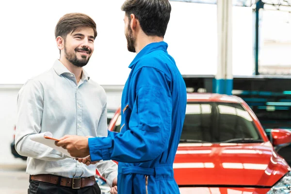 Tamirci kırmızı arabayı kontrol ettikten sonra müşteriyle tokalaşıyor. Mutlu tamirciye ve memnun müşteriye odaklan. Otomobil tamirhanesi. Profesyonel hizmet. Müşteriye odaklan..