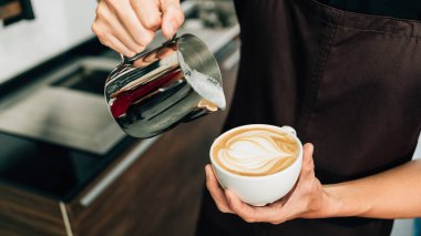 Latte Art yapmak için sıcak espresso sade kahvesine sıcak süt döken genç bir barista görüntüsü..