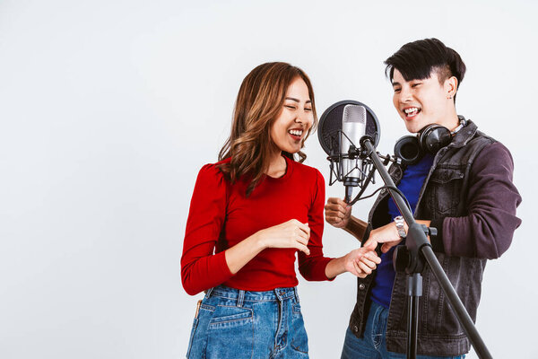 Pretty Asian female and male singers recording songs by using a studio microphone and pop shield on the microphone with passion in music recording studio white background. Duet session.
