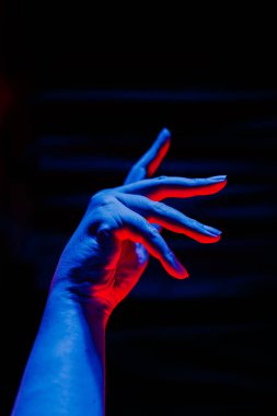 Yakın plan el dansı, arka planda bulanık siyah perde olan mavi ve kırmızı ışıklarla süslenmiş poz verir. Performans, balerin ve diğer danslar için modern el koreografisi.