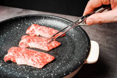 Yüksek mermer desenli bonfile Wagyu A5 bifteği. Siyah arka planda elleri olan bbq maşasıyla mermer kaplı yapışmaz tavayı alıp ızgara yapın. Yakiniku 'ya hizmet ettim..