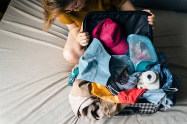 Güneş gözlüğü, polaroid kamera, kozmetik çanta ve küçük çanta gibi dağınık eşyalarına bakan Asyalı kadın bagajdaki her şeyi mücadele ederek sığdırmaya çalışıyor. Kaçış tatiline gitmek için bavul hazırlıyorum..