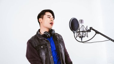 Asyalı erkek şarkıcı bir stüdyo mikrofonuyla şarkı kaydediyor ve mikrofonu tutkulu bir şekilde mikrofona bağlıyor. Müzik sektöründe performans ve gösteri. Kopyalama alanı olan resim.