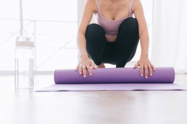 Spor kıyafetleri giymiş, su şişesiyle yoga minderi saran ve yogaya hazırlanan genç bir kadının görüntüsü. Evde ya da yoga stüdyosunda çalışıyorum. Sağlıklı alışkanlıklar, formda kalma, kilo verme kavramları.