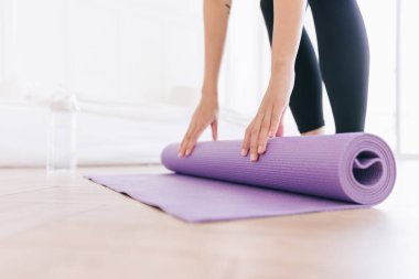 Spor kıyafetleri giymiş, su şişesiyle yoga minderi saran ve yogaya hazırlanan genç bir kadının görüntüsü. Evde ya da yoga stüdyosunda çalışıyorum. Sağlıklı alışkanlıklar, formda kalma, kilo verme kavramları.