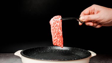 Az pişmiş bonfile Wagyu A5 bifteği, yüksek mermer desenli mermer kaplama yapışmaz tavanın üzerinden siyah arka planda elleri olan bbq maşası ile alınır. Yakiniku 'ya hizmet ettim..