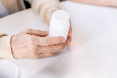 İlaç vermeden önce elinde ilaç şişesi olan ve hemşireden bilgi isteyen yaşlı bir kadının ellerini kapat. Bakıcı eve ziyarete geldi. Ev sağlığı ve huzurevi kavramı.