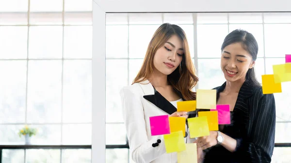 成功したアジアのビジネス女性のチームワークのグループ 新しいアイデアのためのガラスの壁にカラフルな粘着性の紙のノートとのブレインストーミング テクノロジースタートアップオフィスでのビジネスにアジャイル手法を活用 — ストック写真
