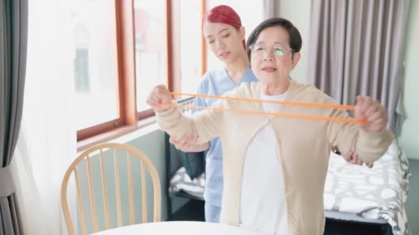 Nurse Caregiver Wearing Scrubs Exercises Senior Asian Woman Using Resistance — Stock Video