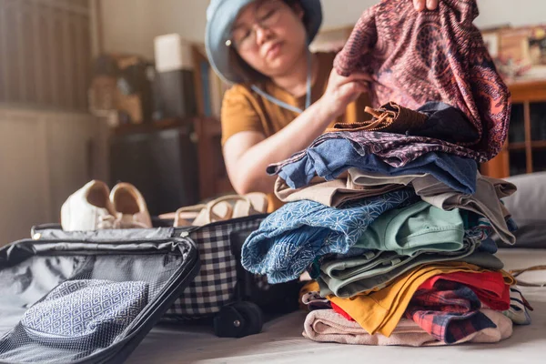 A woman folds clothes from a pile of selected belongings and puts them in luggage on the bed. Packing to go on a getaway vacation. Focus on clothes.