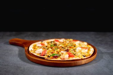 Lezzetli sıcak deniz mahsulleri çıtır çıtır pizza - midye, karides ve kırmızı biberli kani ve erimiş mozzarella peyniri yuvarlak pizza hamuru üzerinde, beton masanın üstündeki ahşap pizza tavasında.