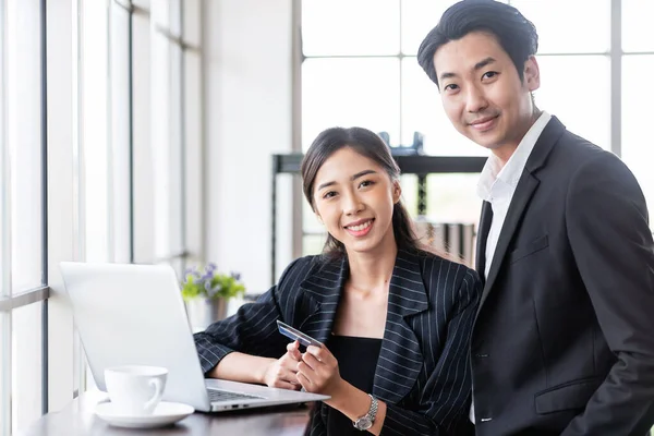 Two Asian business people use a credit card for online payments. Business people shop online, e-commerce, internet banking and spend money with security and confidence.