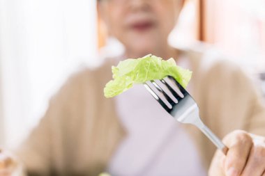 Close-up of fresh and clean lettuce Poke with a fork from a vegetarian salad served to a senior female patient at home. Caregiver visit at Home. Home health care concept and nursing home.