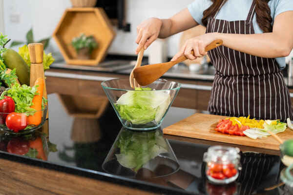 Close up hands of Asian woman wearing apron, tossing the vegetarian salad with wooden spatulas. Preparing a healthy salad with fresh vegetables such as carrot, tomato cabbage and green oak.